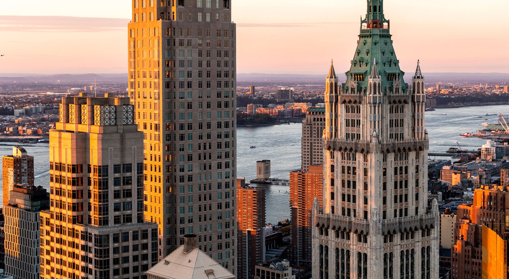 Golden sunset illuminating NYC skyscraper from 19 Dutch, with the Woolworth Building and river views in the background.