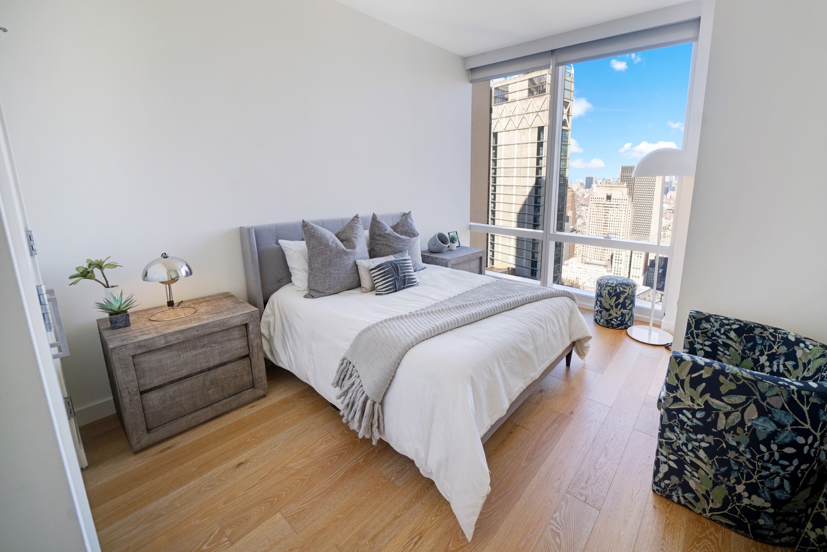 Bright bedroom at 19 Dutch with large bed, warm wood floors, and expansive skyline views overlooking Lower Manhattan.