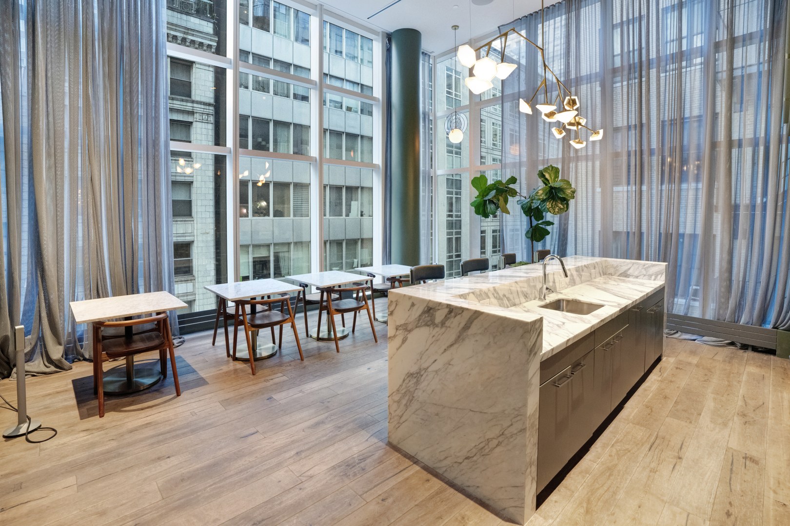 Bright communal kitchen at 19 Dutch featuring marble island, high ceilings, café seating, and floor-to-ceiling windows.