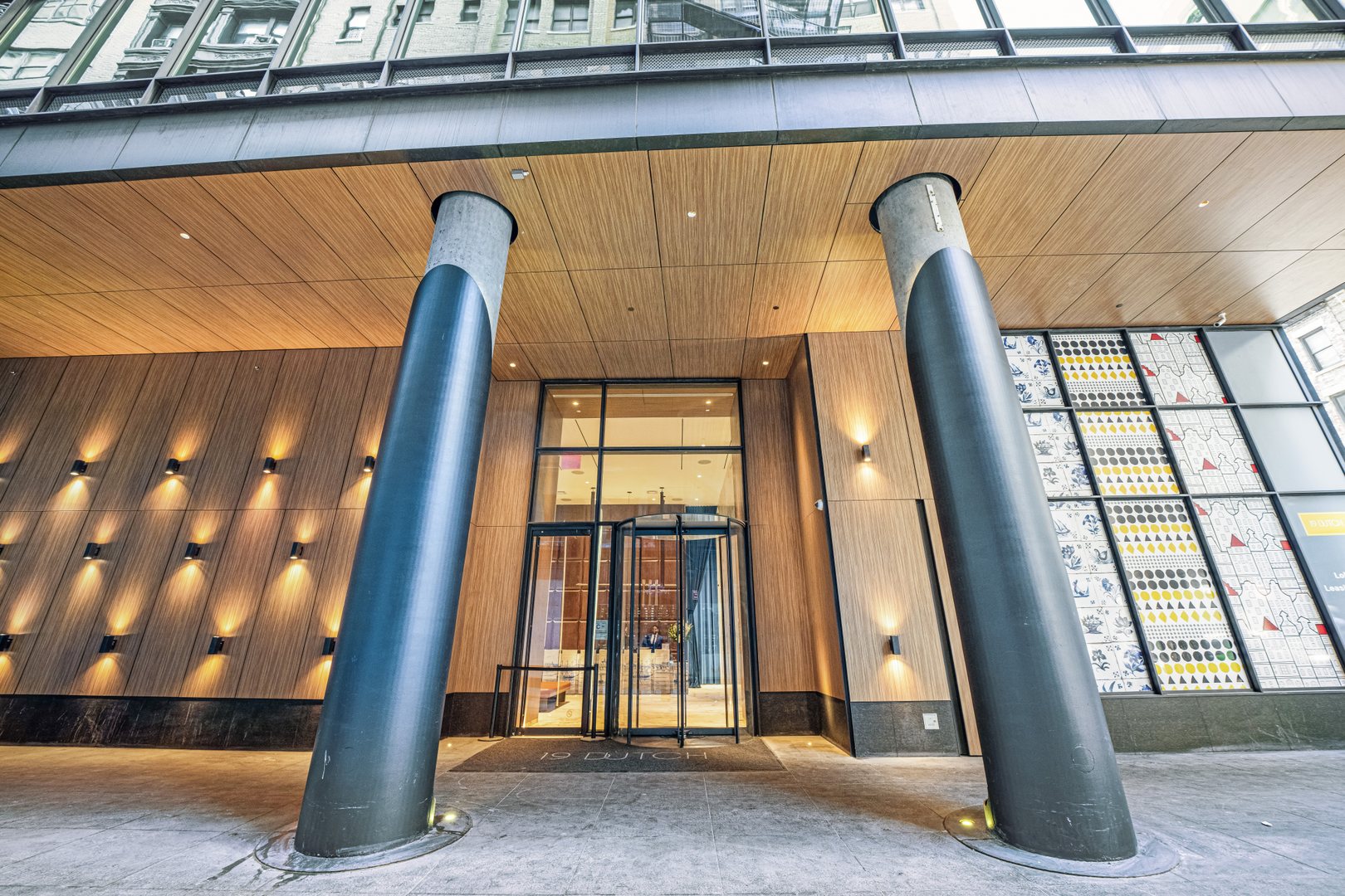 19 Dutch building entrance with tall angled columns, wood-paneled façade, and a glass revolving door.
