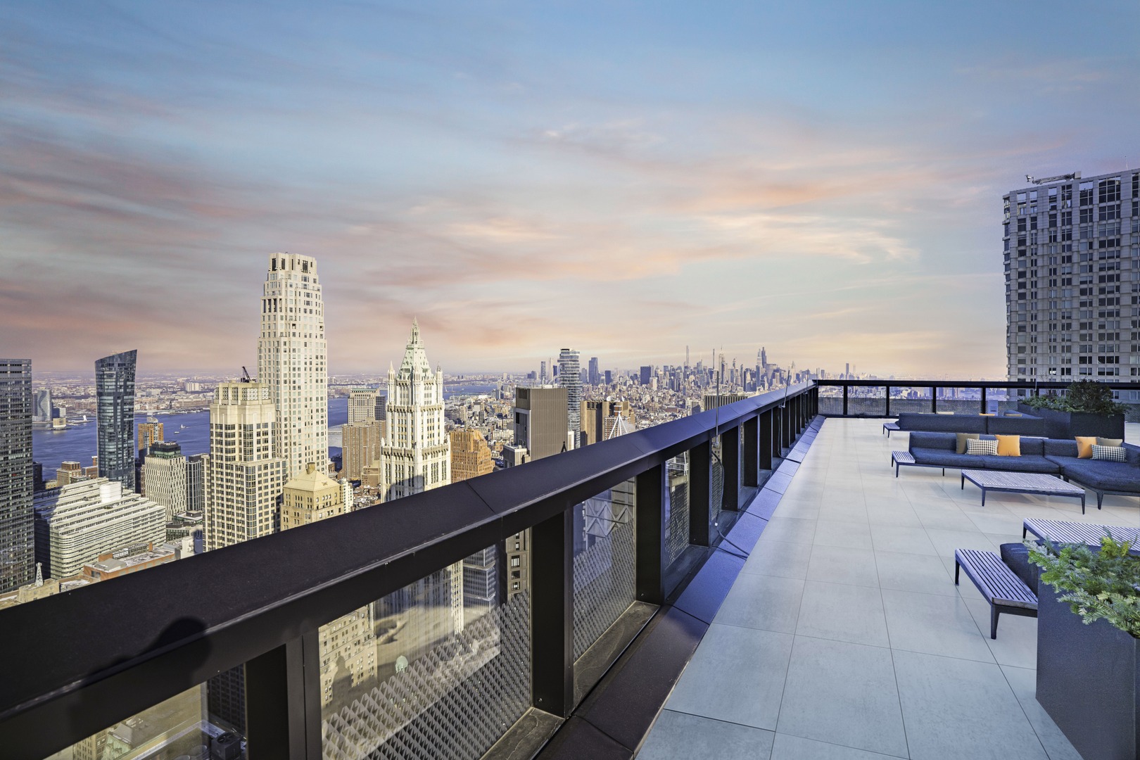 Rooftop terrace with lounge seating and panoramic skyline views of Lower Manhattan at sunset.